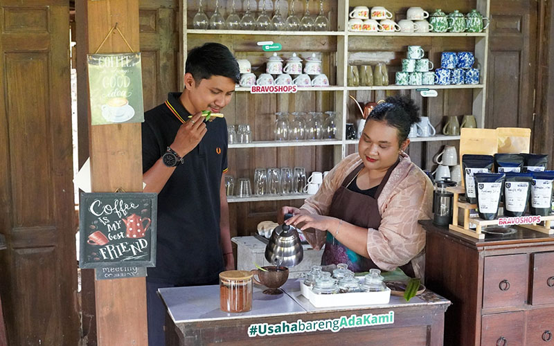 Two people preparing and tasting coffee at a small café counter with coffee products on display.